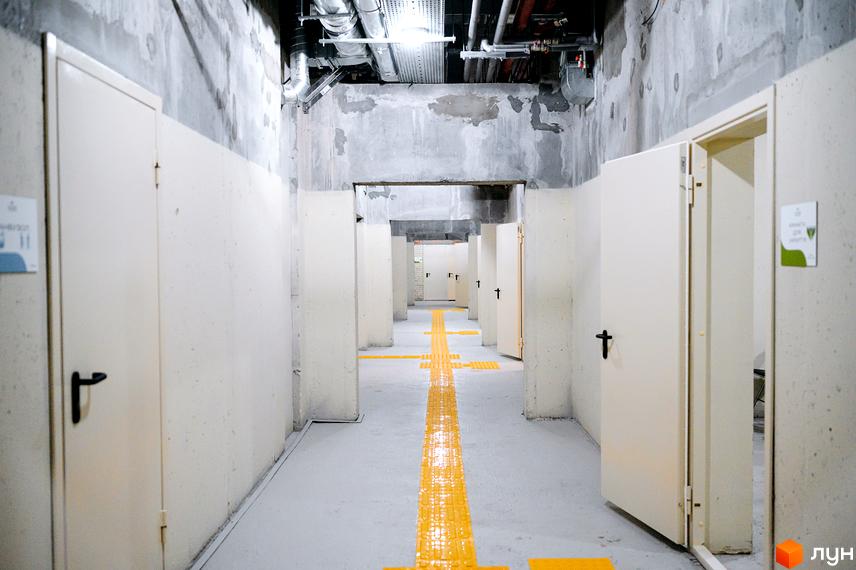 Функціональний коридор Житлового комплексу OXFORD з бетонними стінами, численними дверима та жовтою тактильною розміткою для навігації.