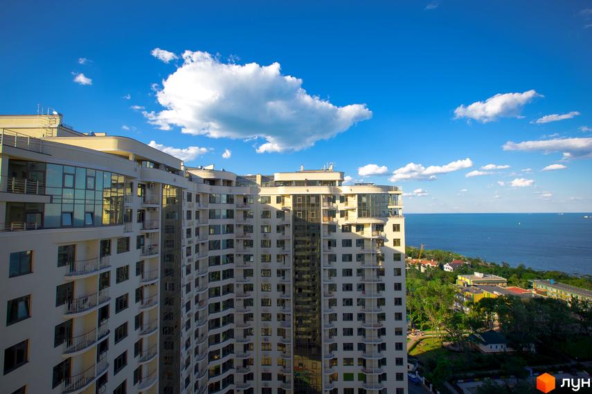 Висотна будівля ЖК Друга Перлина з панорамними вікнами та балконами. На задньому плані видно море та блакитне небо з хмарами.