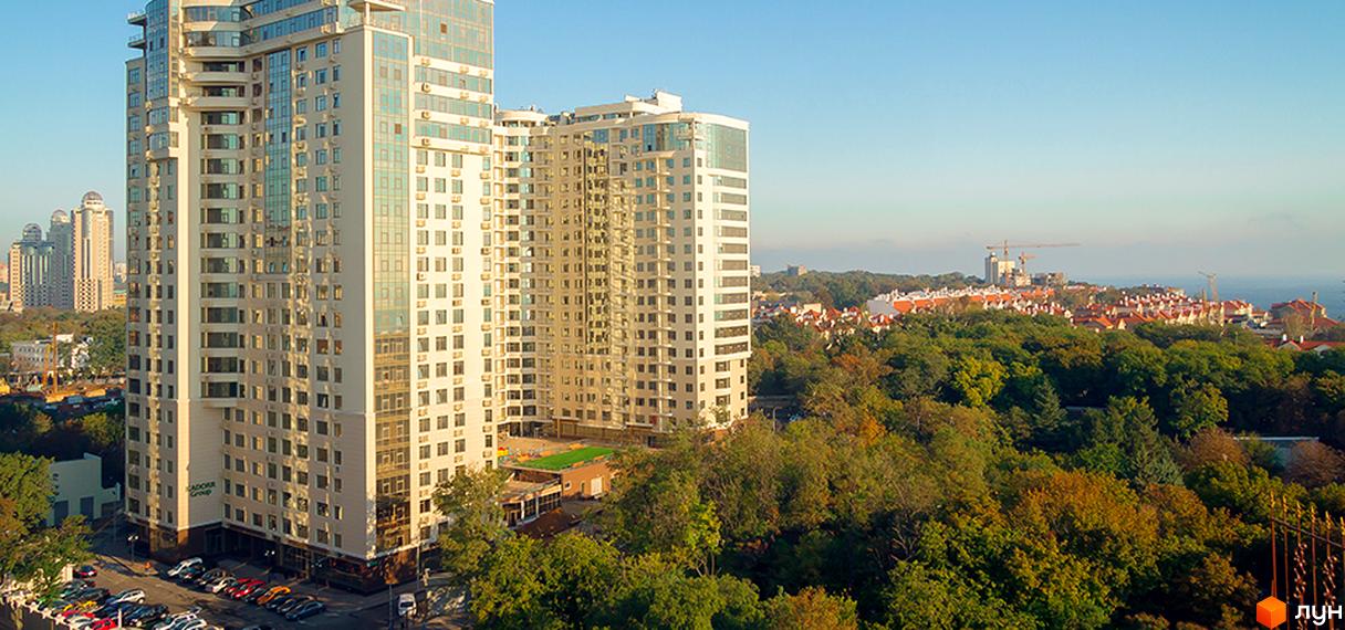 Високі будинки ЖК Друга Перлина з великою кількістю вікон. На прибудинковій території є парковка для автомобілів та зелені насадження.