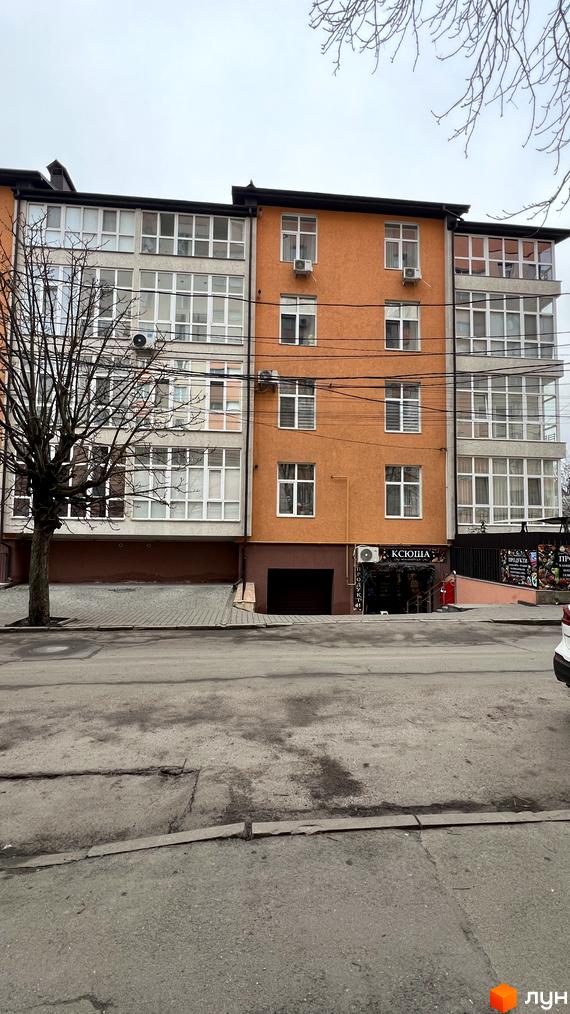 Житловий комплекс на вул. Заболотного, 20, з фасадом оранжевого кольору та великими вікнами. Прибудинкова територія з асфальтованою парковкою.