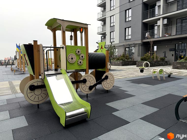 Дитячий майданчик з ігровими елементами у житловому комплексі Park Residence, прибудинкова територія з плиткою.