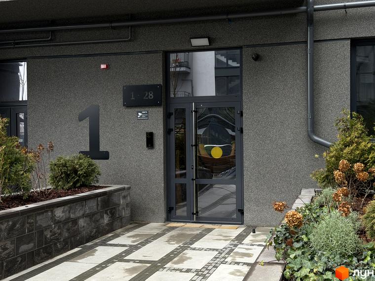 Вхід до будинку житлового комплексу Park Residence з сучасними елементами дизайну та озелененням прибудинкової території.