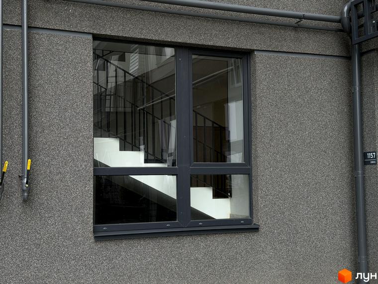 Вікно будинку ЖК Park Residence з видом на сходи всередині. Сіра фактурна стіна та трубопроводи на фасаді.