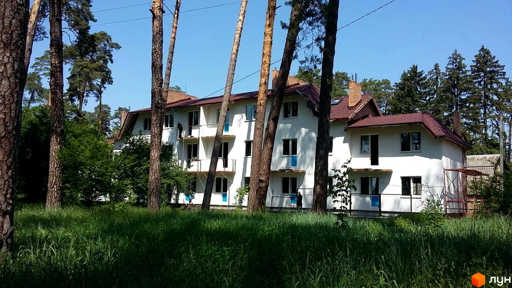 Зображення житлового комплексу Лісова пісня. Білий будинок з коричневим дахом на тлі зелені та дерев.