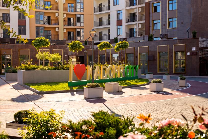 Житловий комплекс KADORR City з сучасними фасадами та прибудинковою територією, озелененою деревами та квітами.