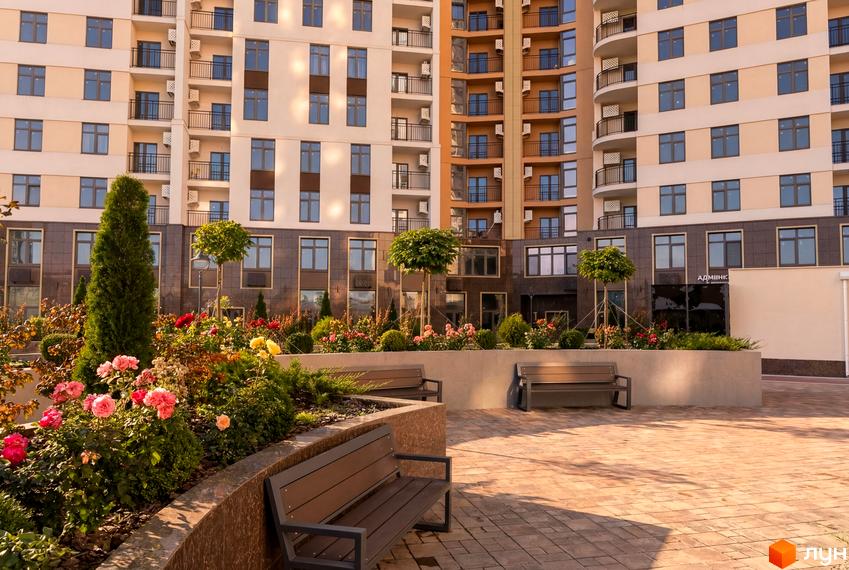 Зовнішній вигляд житлового комплексу KADORR City з квітучою прибудинковою територією та лавками для відпочинку.