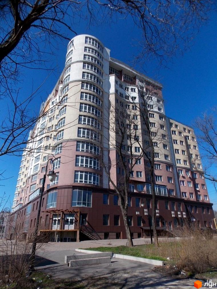 Висотна будівля житлового комплексу Лермонтово з великою кількістю вікон. На передньому плані видно дерева та частину прибудинкової території з тротуаром.