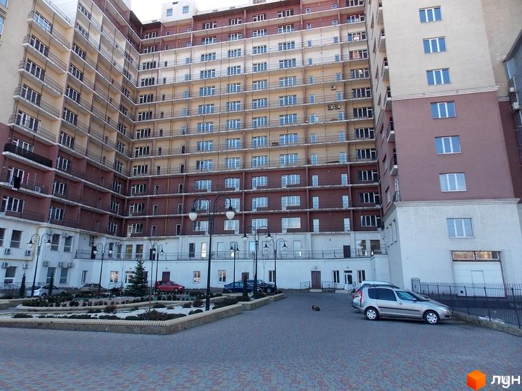 Багатоповерховий будинок ЖК Лермонтово з великою кількістю вікон. На передньому плані облаштована прибудинкова територія з рослинами та місцями для паркування.