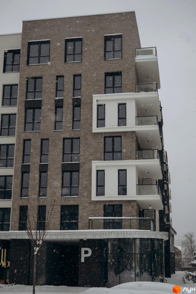 Житловий комплекс SKY CITY з сучасним фасадом та балконами. Прибудинкова територія засніжена, з озелененням та паркувальними місцями.