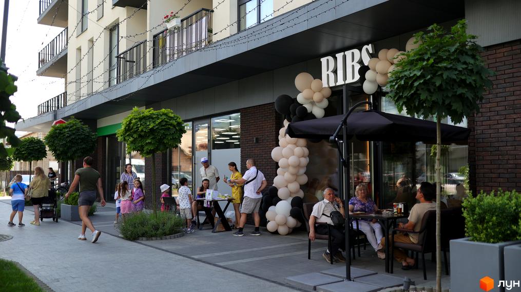 Зовнішній вигляд житлового комплексу SKY CITY з кафе на першому поверсі та прибудинковою територією з зеленими насадженнями.