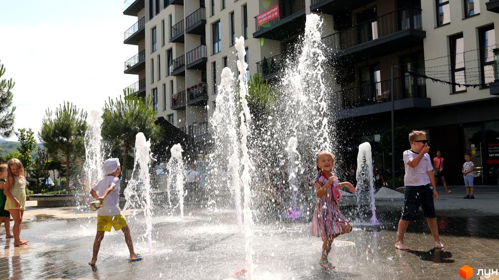 Сучасний житловий комплекс SKY CITY з фонтаном на прибудинковій території, де діти грають у воді.
