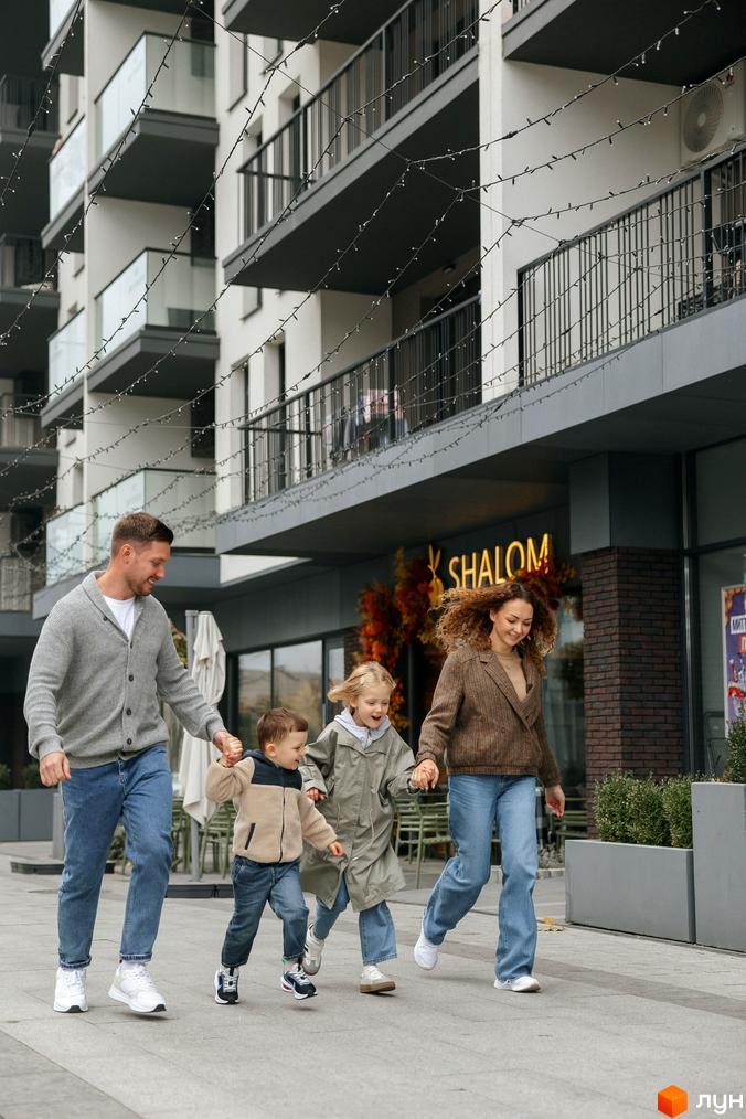 Житловий комплекс SKY CITY з балконами та прибудинковою територією, де сім'я гуляє по тротуару.