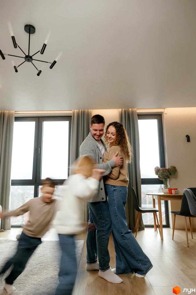 Сім'я щасливо проводить час у сучасній квартирі з великими вікнами. Внутрішній інтер'єр з дерев'яною підлогою та стильними меблями.