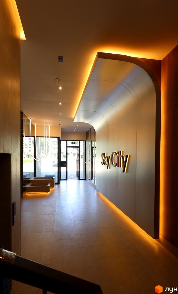 Житловий комплекс SKY CITY: інтер'єр вхідної групи з м'яким освітленням, вигнутою стіною з логотипом та панорамними вікнами.