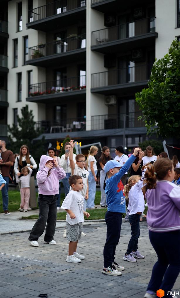 Житловий комплекс SKY CITY з балконами та зеленими насадженнями. Діти грають на прибудинковій території з травою та плиткою.
