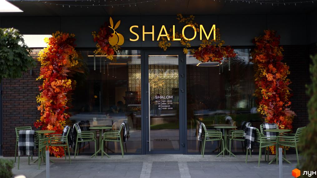 Вхід до закладу Shalom з яскравим оформленням та зеленими столиками на прибудинковій території. Осінні декорації на фасаді створюють затишну атмосферу.