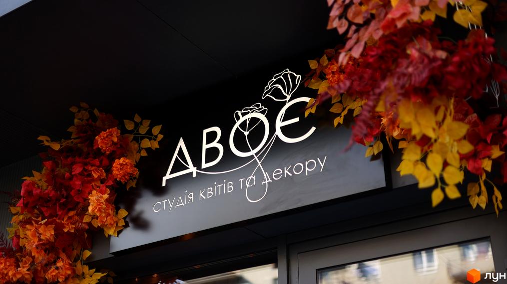 Вивіска студії квітів та декору з яскравими осінніми квітами на фоні. Сучасний фасад з елементами декору.