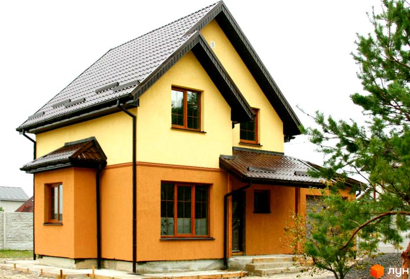 Двоповерховий будинок Котеджного містечка Приозерний з коричневим дахом, світло-жовтими та помаранчевими стінами, оточений зеленою сосною.