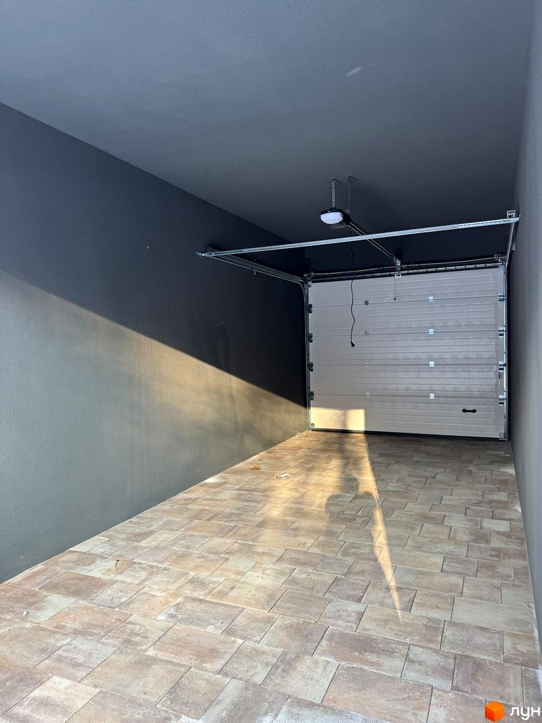 Внутрішній вигляд гаража житлового комплексу Madera House з плитковою підлогою та автоматичними воротами.