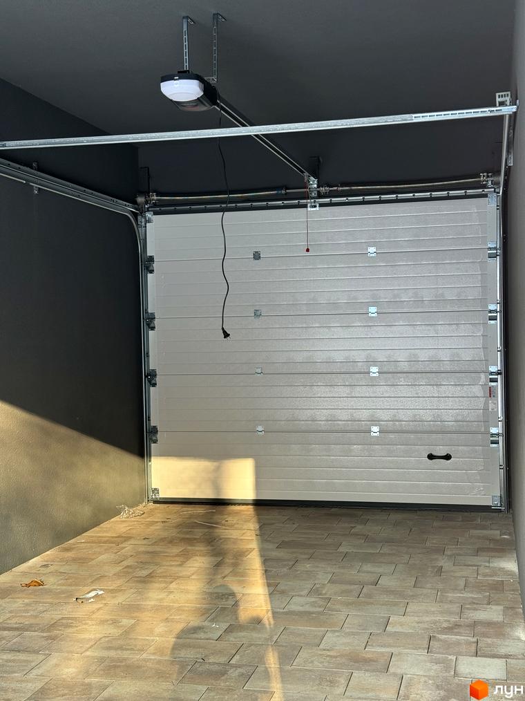 Таунхауси Madera House з білими секційними воротами та бруківкою на підлозі. Зовнішній вигляд будинку та прибудинкової території.