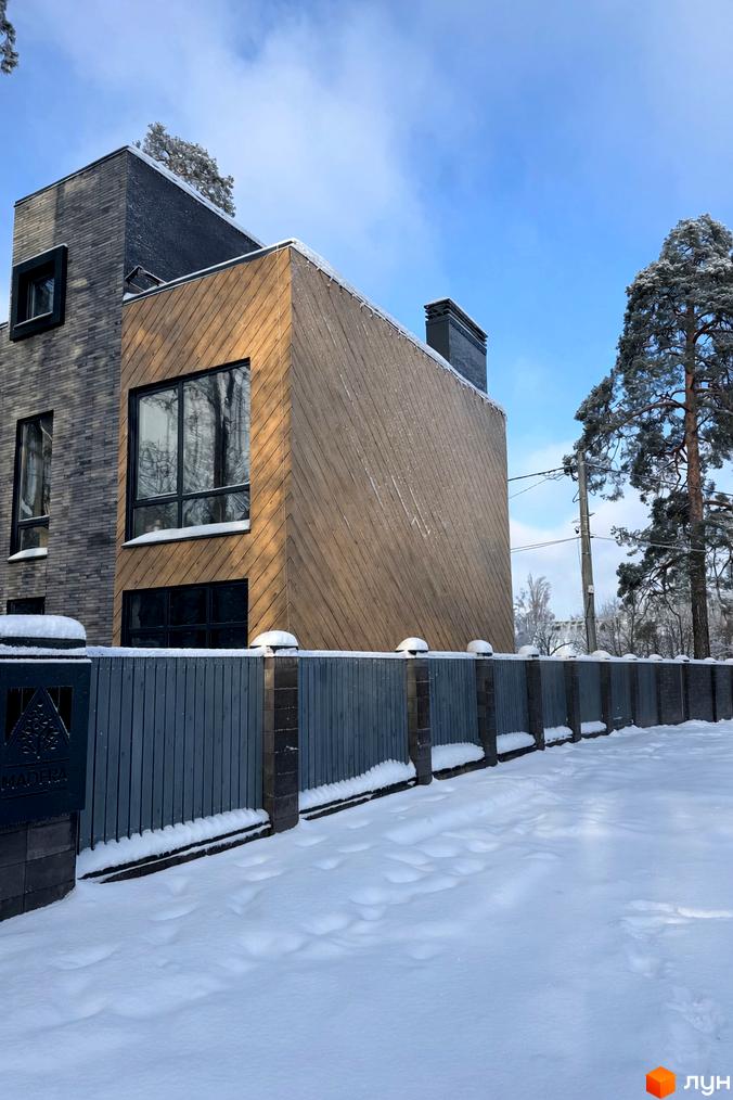 Сучасний будинок житлового комплексу Madera House з дерев'яними та цегляними елементами. Прибудинкова територія вкрита снігом з огорожею.