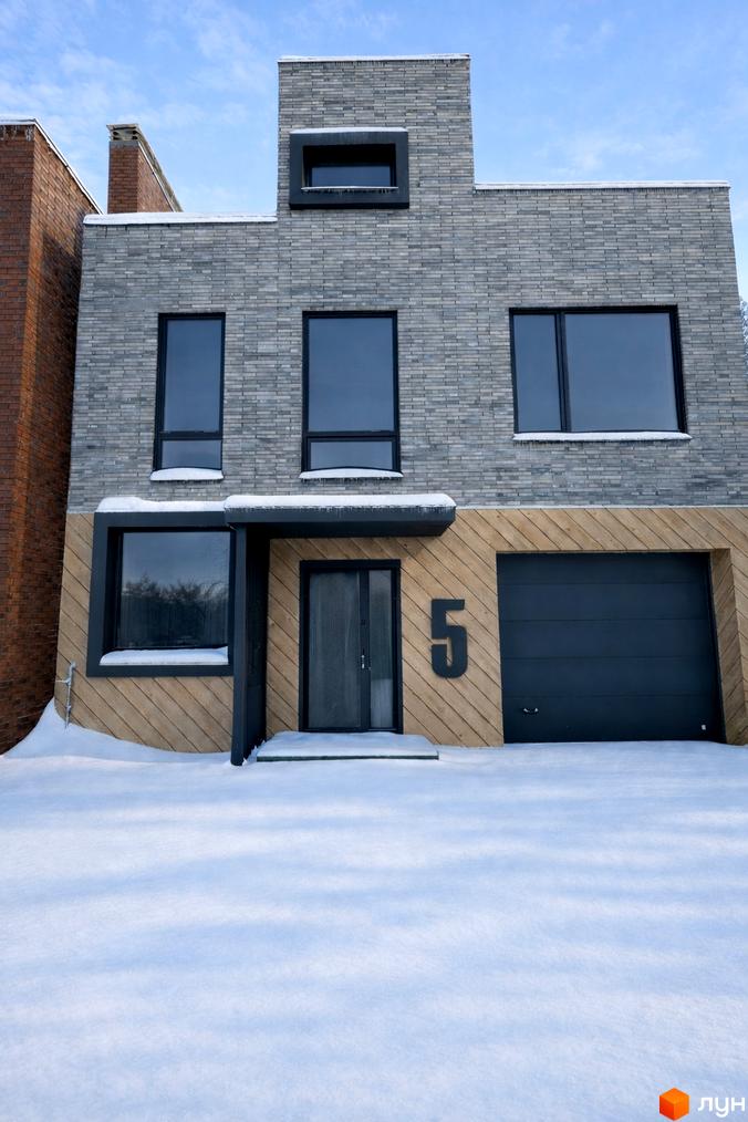 Таунхауси Madera House – сучасний будинок з дерев'яним оздобленням та гаражними воротами, оточений снігом. Зовнішній вигляд будинку та прибудинкової території.