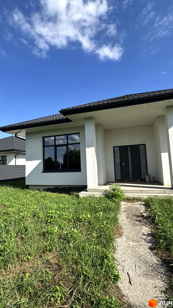 Будинок житлового комплексу КМ Котеджі на Київській з великими вікнами та входом. Прибудинкова територія з зеленими насадженнями та доріжкою.