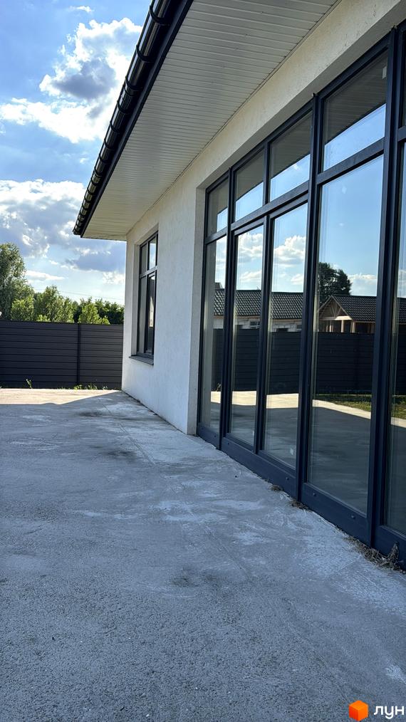 Зовнішній вигляд будинку житлового комплексу КМ Котеджі на Київській з великими вікнами. Прибудинкова територія з бетонною підлогою та огорожею.