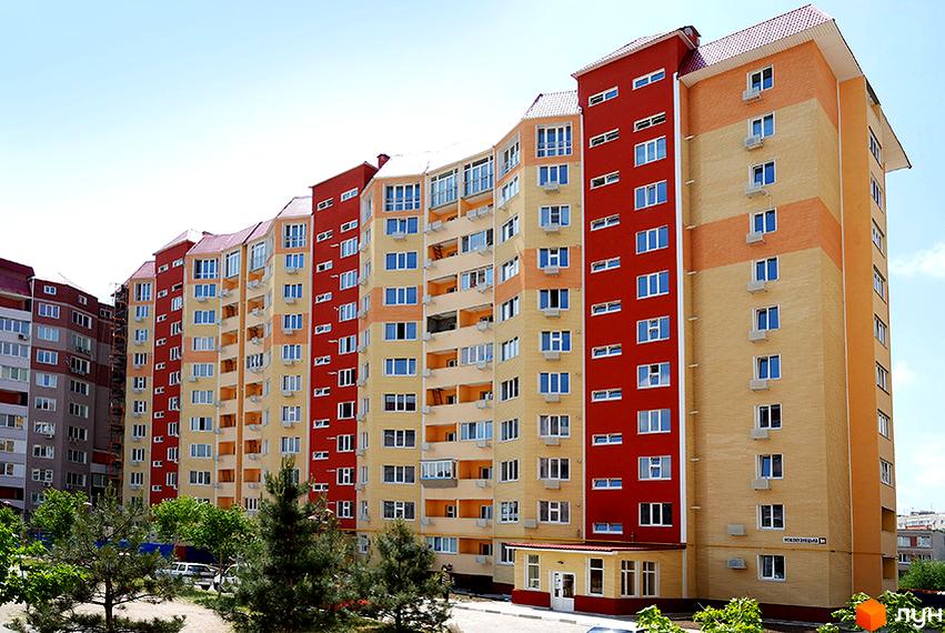 Житловий комплекс Рассвет-1 з червоними та жовтими фасадами, численними вікнами та балконами. На передньому плані видно зелені дерева та доріжки.