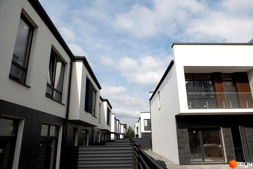 Сучасні таунхауси SDG BILOHORODKA 2 з білими фасадами та великими вікнами, прибудинкова територія з зеленими насадженнями.