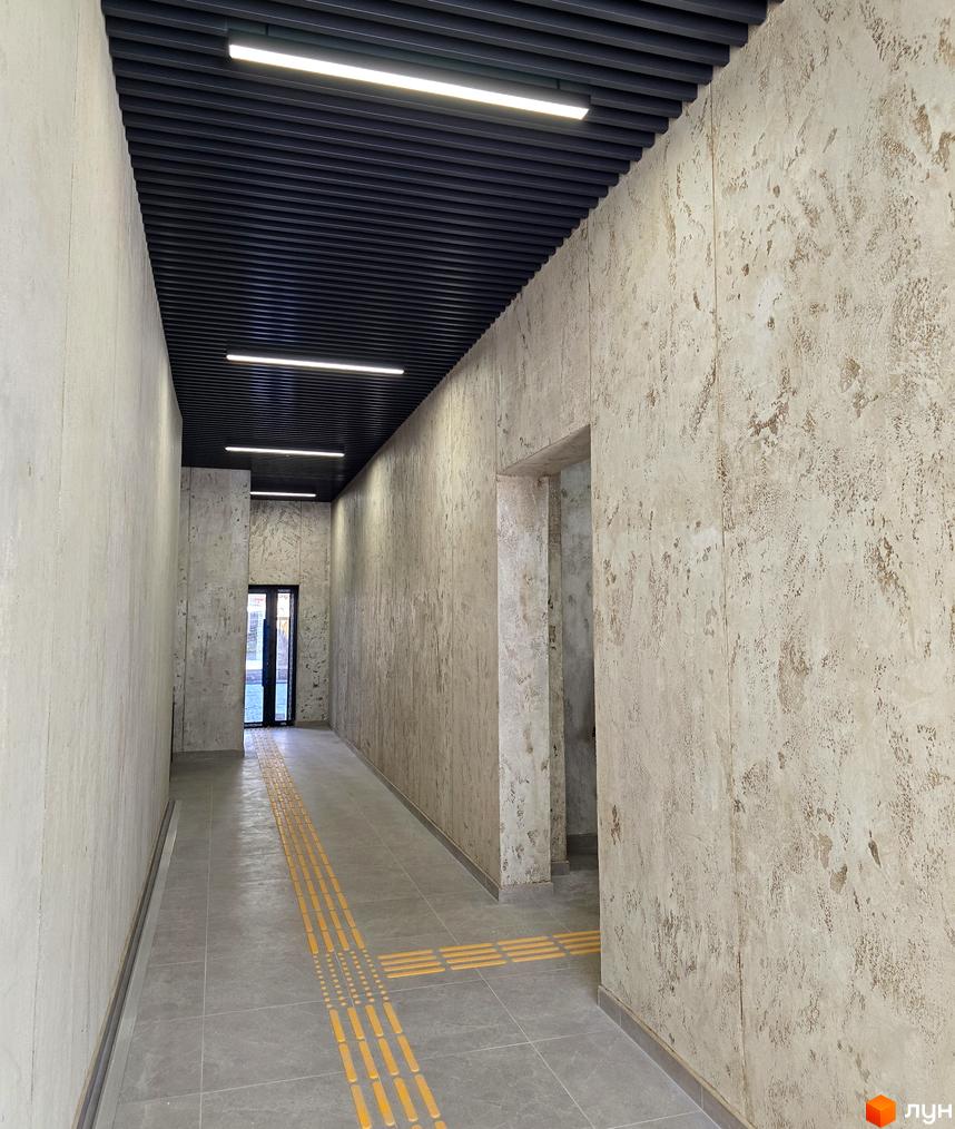 Сучасний коридор житлового комплексу ЖК КОРОНА з освітленням та плитковою підлогою. Стіни оздоблені світлими матеріалами.