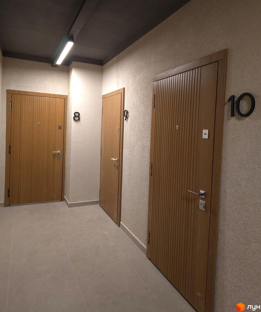 Коридор житлового комплексу ЖК КОРОНА з дерев'яними дверима квартир та сучасним освітленням.