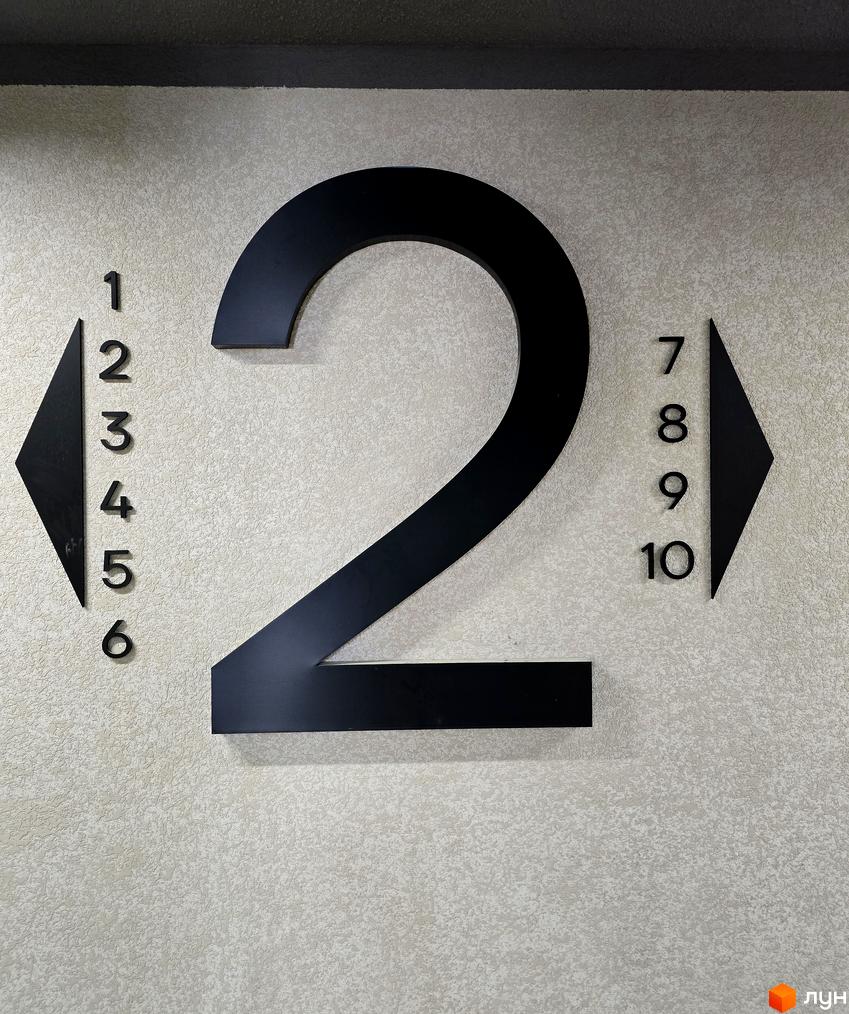 Номер поверху 2 на стіні з текстурованим покриттям, поруч розташовані позначення для ліфта.