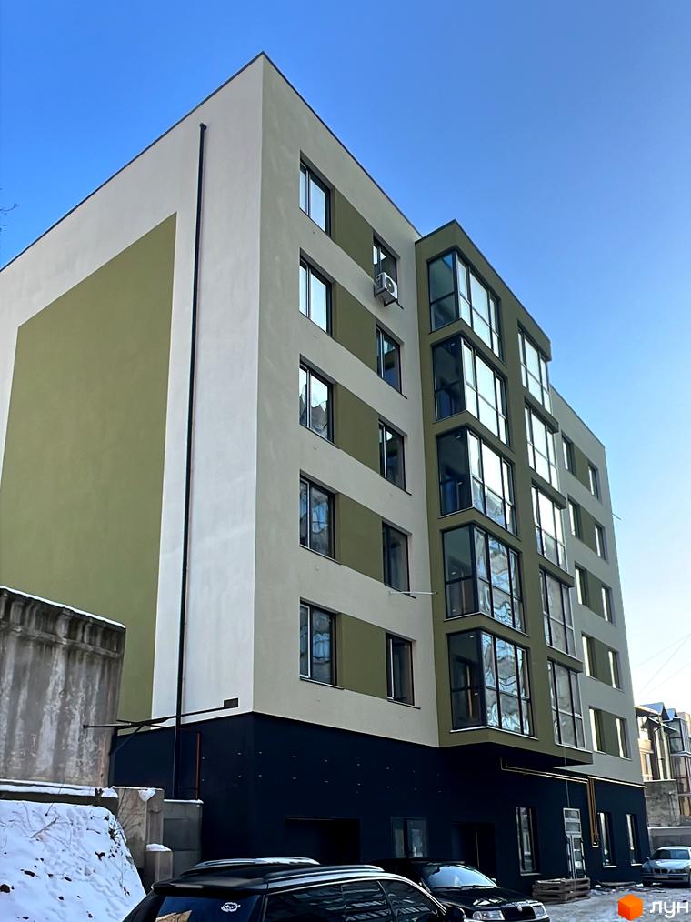 Житловий комплекс на вул. Заболотного з фасадом у світлих тонах та великими вікнами. Прибудинкова територія з автомобілями та засніженими ділянками.
