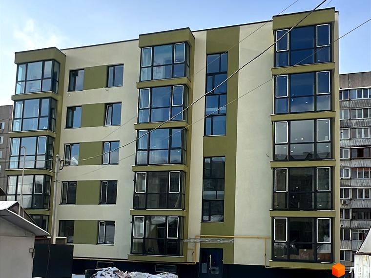 Зовнішній вигляд будинку на вул. Заболотного з великими вікнами та сучасним фасадом. Прибудинкова територія з невеликими будівельними матеріалами.