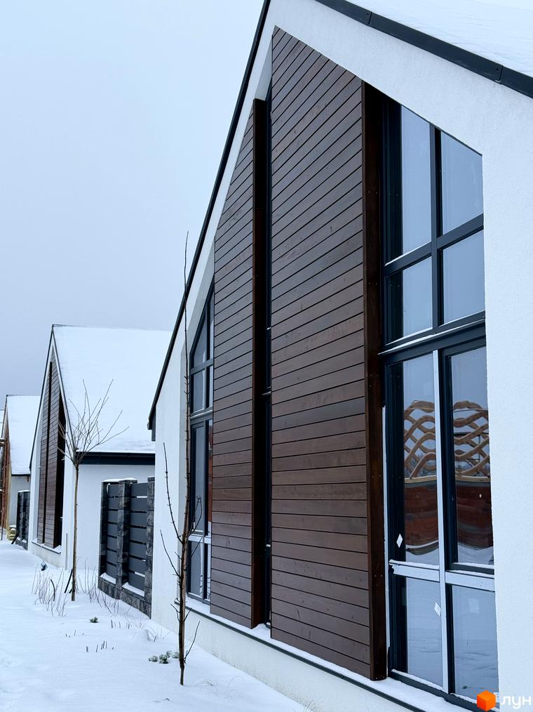 Будинок житлового комплексу КМ Ovillas з дерев'яними елементами фасаду. Прибудинкова територія з снігом та молодими деревами.