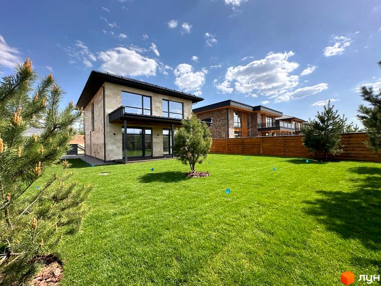 Будинок житлового комплексу КМ Нова Ходосівка з великими вікнами та прибудинковою територією, обрамленою зеленими насадженнями.