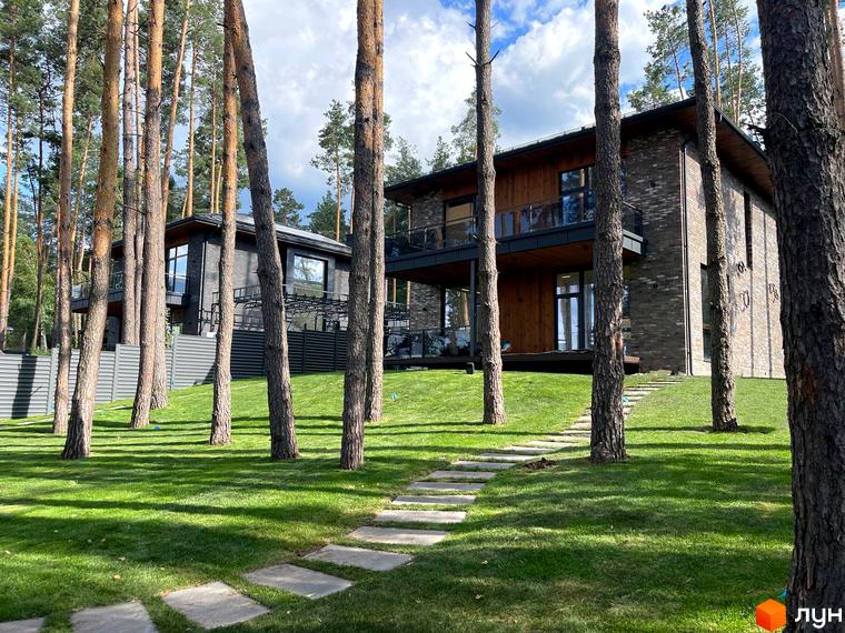 Зовнішній вигляд котеджного комплексу КМ Нова Ходосівка з зеленими газонами та доріжками, оточений соснами.