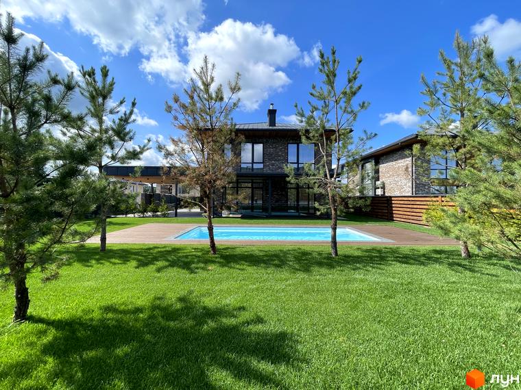 Зовнішній вигляд будинку житлового комплексу КМ Нова Ходосівка з басейном та зеленим газоном. Прибудинкова територія з деревами та ландшафтним дизайном.