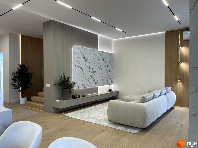 Сучасний інтер'єр вітальні з м'яким диваном, дерев'яними сходами та декоративними елементами. Простора кімната з натуральним освітленням.