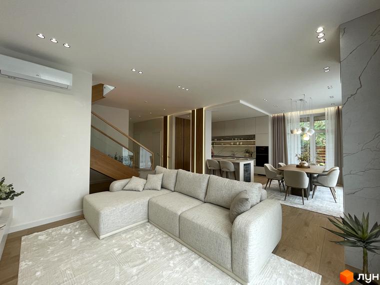 Сучасна вітальня з м'яким диваном та обідньою зоною в житловому комплексі КМ Нова Ходосівка. Простора кімната з великими вікнами та світлом.