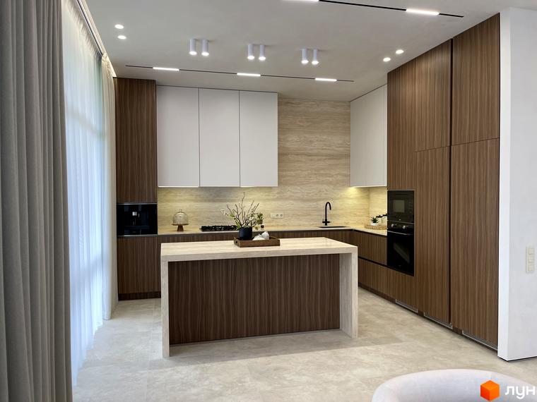 Сучасна кухня з дерев'яними фасадами та світлими стінами, з островом та технікою. Вікна з шторками пропускають природне світло.