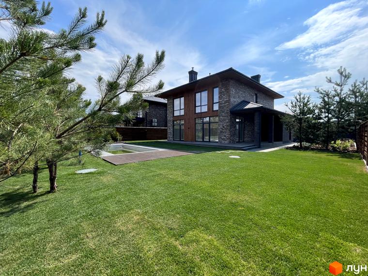 Зовнішній вигляд будинку КМ Нова Ходосівка з прибудинковою територією, зеленим газоном та деревами.