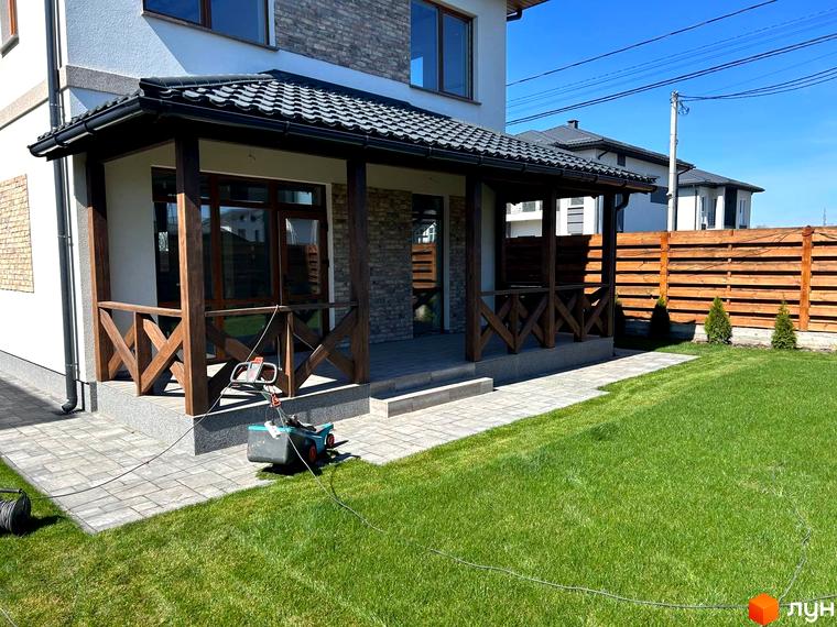 Зовнішній вигляд будинку з верандою у Комплекс Озерний, прибудинкова територія з газоном та мощенням.