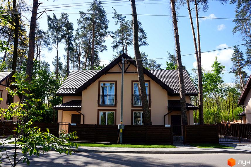 Двоповерховий будинок світло-коричневого кольору з коричневим дахом та вікнами в Котеджному містечку Sweet Home. Оточений високими соснами та дерев'яним парканом.