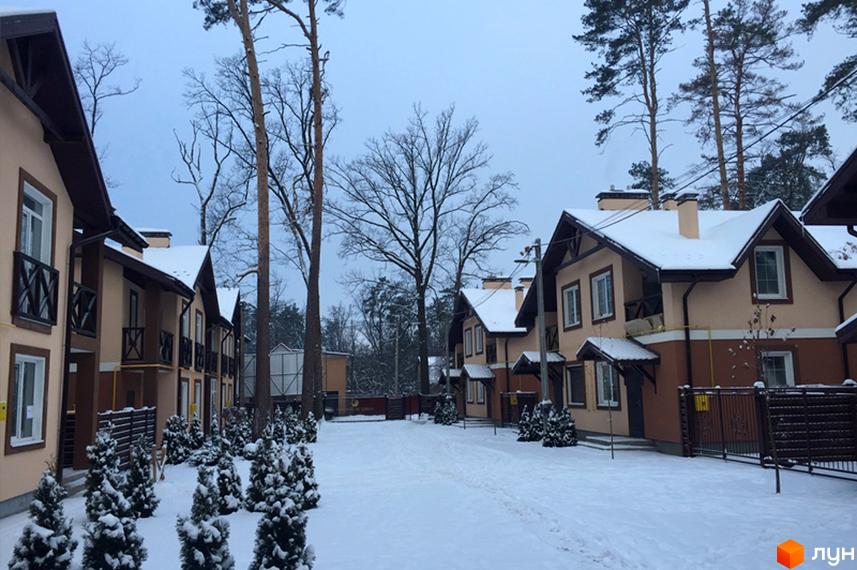 Котеджне містечко Sweet Home взимку: двоповерхові будинки з бежево-коричневими фасадами та засніженими дахами, оточені засніженими деревами та кущами.