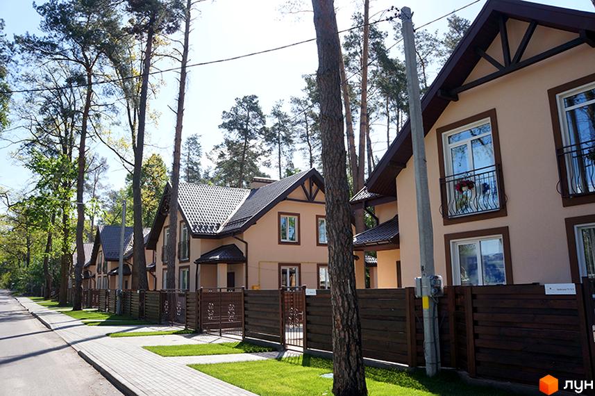 Котеджне містечко Sweet Home: будинки світлого кольору з темними дахами, декоративними елементами та балконами. Вулиця з тротуаром, зеленими газонами та високими деревами.