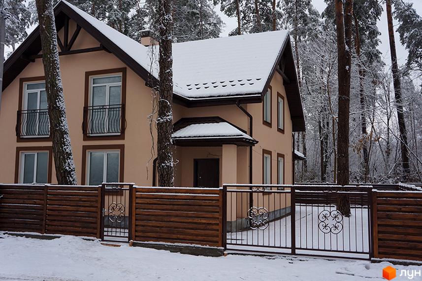 Будинок КМ Sweet Home з бежевим фасадом, темним дахом та балконами взимку. Засніжена територія з дерев'яною огорожею та металевими воротами.