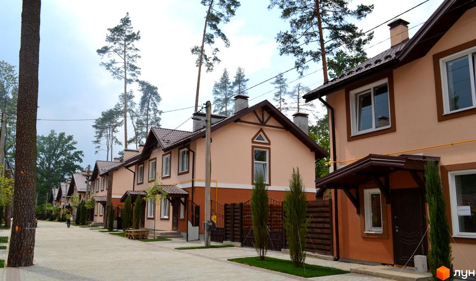 Котеджне містечко Sweet Home: ряд двоповерхових будинків персикового кольору з коричневими дахами та білими вікнами. Вулиця з бруківки та зелені насадження.