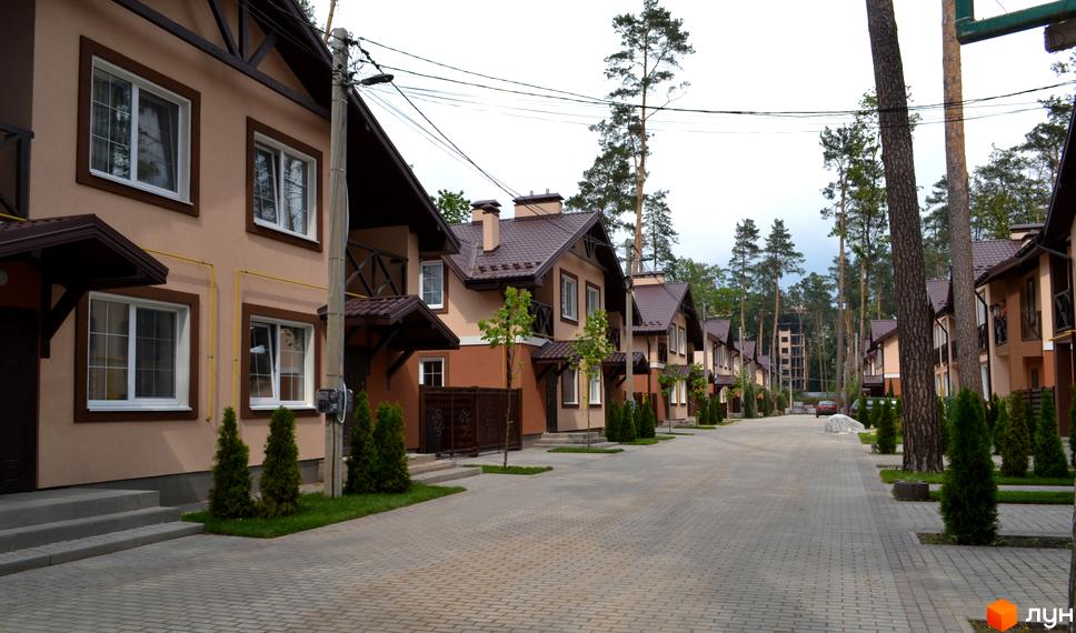 Котеджне містечко Sweet Home: ряд двоповерхових будинків з коричневими дахами та світлими фасадами. Вулиця з бруківки оточена деревами та зеленими насадженнями.